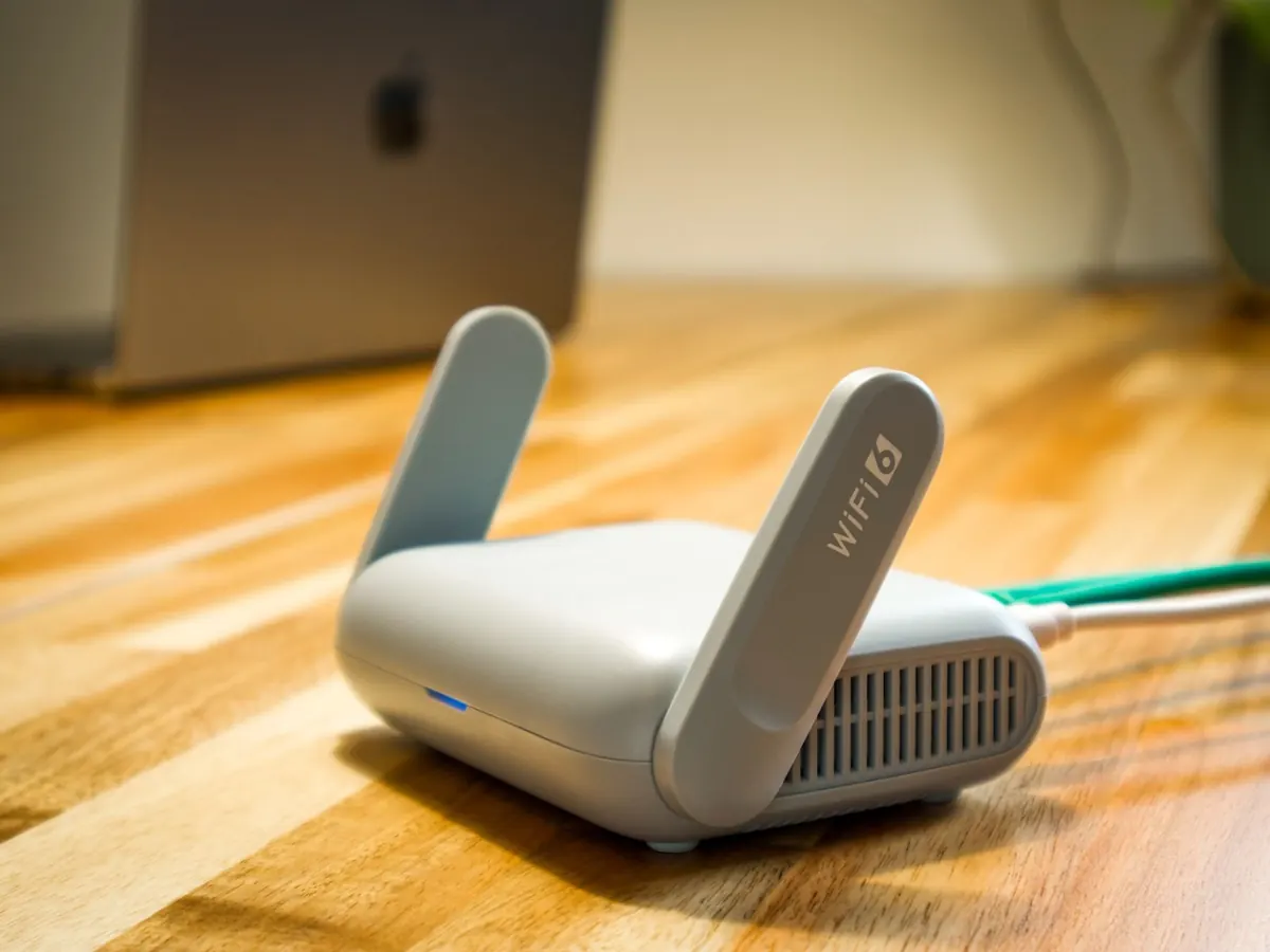 Roteador Wi-Fi com duas antenas sobre uma mesa de madeira, ligado por cabo de rede